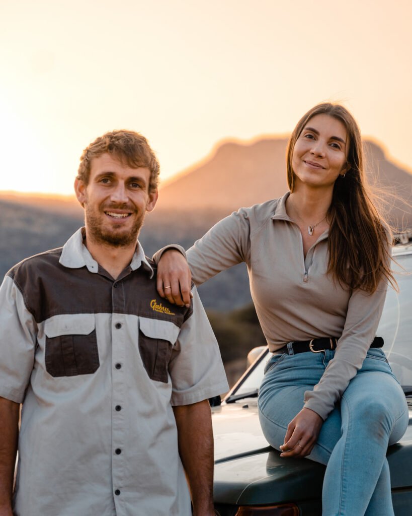 A photo of the owners of Mangetti Travel Agency Namibia posing in front of the sun setting behind the mountains